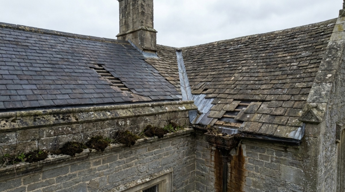 Aerial view of a listed stone building roof with a rippled lead valley and a moss-filled parapet gutter